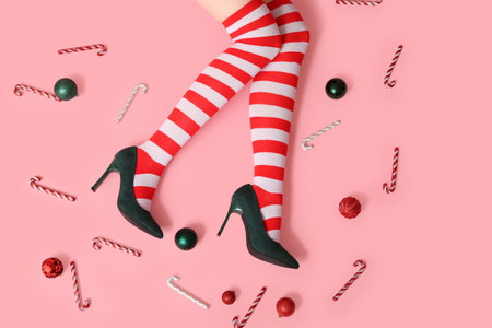 Legs of young woman in striped stockings with Christmas balls and candy canes on pink backgroundの写真素材