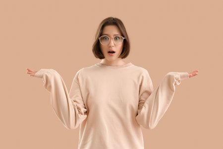 Wondering young woman shrugging on beige backgroundの写真素材