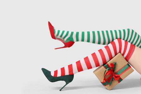 Legs of young woman in different striped stockings with gift box on gray background. Christmas celebrationの写真素材