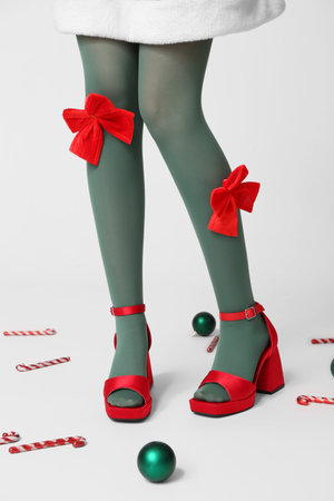 Legs of young woman in green tights with bows, Christmas balls and candy canes on gray background