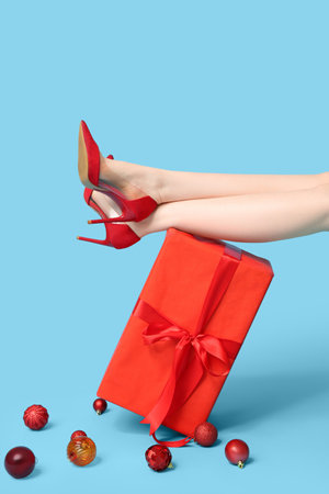 Legs of young woman in red high heels with gift boxes and Christmas balls on blue backgroundの写真素材