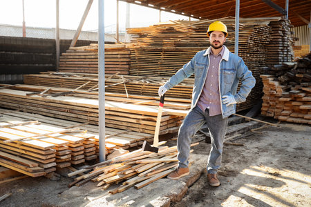Male carpenter in hardhat with ax at sawmill