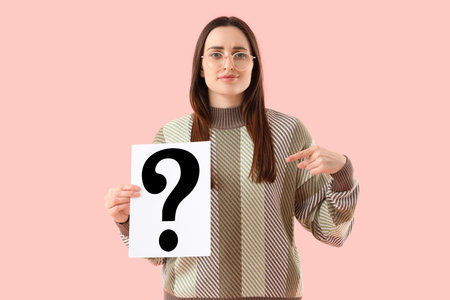 Young woman pointing at paper question mark on pink background