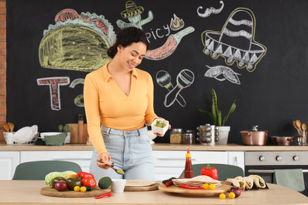 Young African-American woman making tasty taco with guacamole at table in kitchenの写真素材