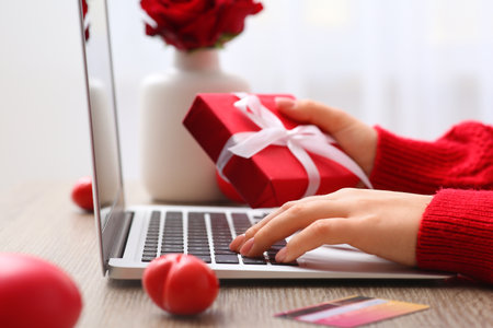 Woman with gift box, credit card and modern laptop at table. Valentine's Day celebrationの写真素材