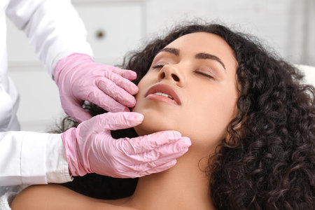 Beautiful young African-American woman receiving facial massage in beauty salon, closeup