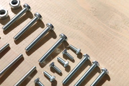 Arrangement of tap bolts and chrome nuts on wooden background