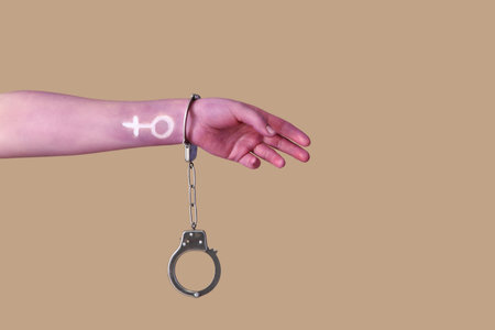 Painted female hand with handcuffs on brown background. Feminism concept