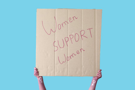 Woman holding placard with text WOMEN SUPPORT WOMEN on blue background. Feminism conceptの写真素材