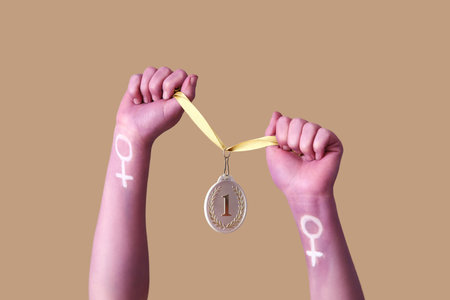 Woman with painted hands holding first place medal on brown background. Feminism conceptの写真素材