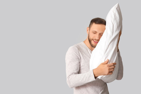 Young man in pajamas with soft pillow on gray background. World Sleep Dayの写真素材