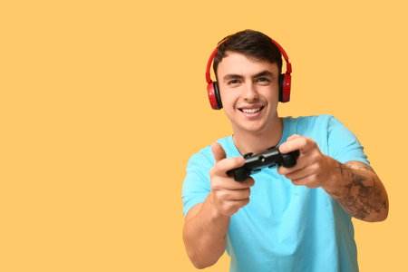 Handsome young man in headphones playing video games on yellow background