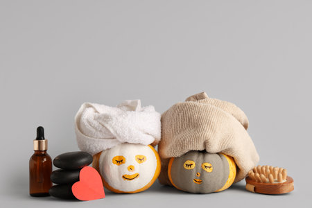 Funny pumpkins with facial masks, towels, spa accessories and red heart on gray backgroundの写真素材
