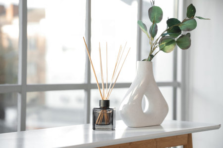 Reed diffuser and vase with eucalyptus branches on table near window in living room, closeupの写真素材