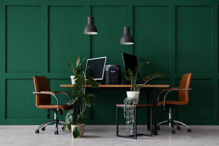 Workplace with computer monitors, portable power station and plants near green wall in officeの写真素材