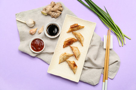 Plate with fried Japanese gyoza and bowls of sauces on lilac backgroundの写真素材