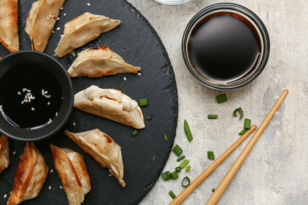 Black board with fried Japanese gyoza and bowls of soy sauce on gray backgroundの写真素材