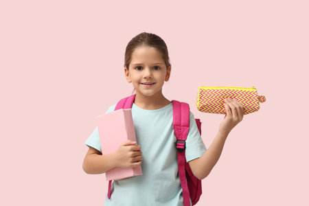 Cute little happy girl with backpack, pencil case and book on pink backgroundの写真素材