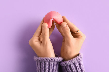 Female hands with pink fortune cookie on lilac backgroundの写真素材