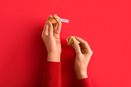Female hands with broken fortune cookie on red backgroundの写真素材