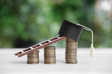 Stacks of coins with graduation hat and ladder on table outdoors. Student loan conceptの写真素材