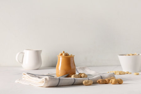 Jar of tasty peanut butter with spoon and nuts on white backgroundの写真素材