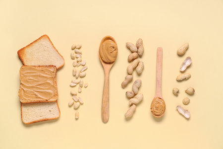 Wooden spoons with tasty peanut butter, toasts and nuts on beige backgroundの写真素材