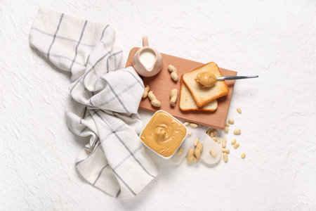 Bowl with tasty peanut butter, jug of milk, toasts and nuts on white background