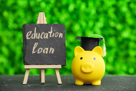Chalkboard with text EDUCATION LOAN and piggy bank on table outdoorsの写真素材