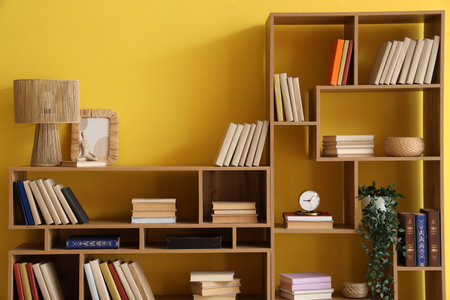 Wooden bookshelves with lamp and decor near yellow wallの写真素材