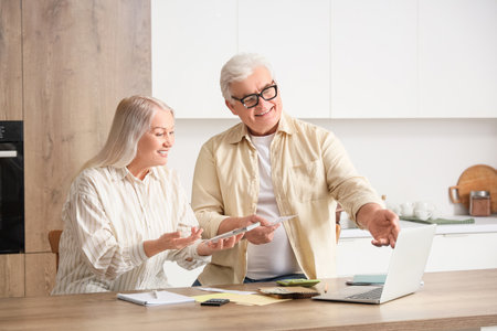 Senior couple with laptop calculating utility bills in kitchenの写真素材