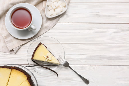 Glass plate with piece of sweet vanilla cheesecake and cup of tea on white wooden backgroundの写真素材