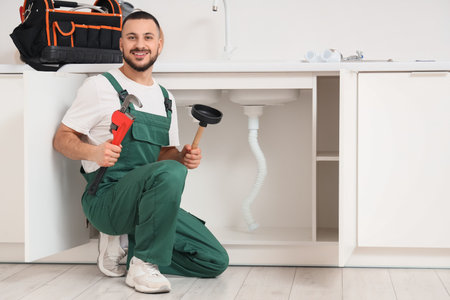 Male plumber with pipe wrench and plunger near sink in kitchenの写真素材