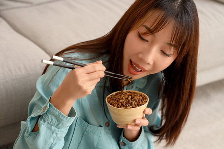 Young Asian woman with chopsticks eating fried insects at home, closeupの写真素材