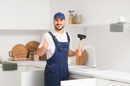 Male plumber with plunger showing thumb-up near sink in kitchenの写真素材