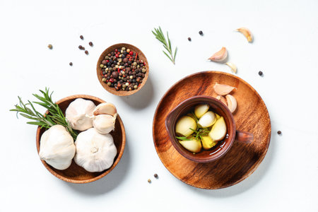 Jug of fresh garlic oil with rosemary and peppercorns on white backgroundの写真素材