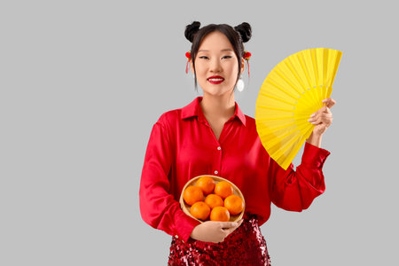 Beautiful Asian woman with paper fan and tangerines on gray backgroundの写真素材