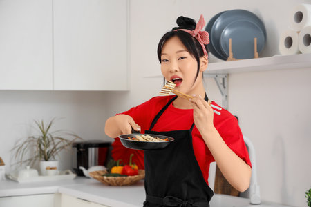 Young Asian woman eating tasty tofu in kitchenの写真素材
