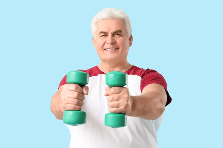 Sporty man senior exercising with dumbbells on blue backgroundの写真素材