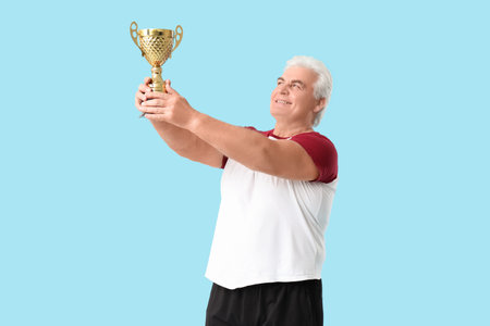 Sporty man senior with gold cup on blue backgroundの写真素材