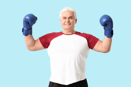 Sporty man senior with boxing gloves showing muscles on blue background