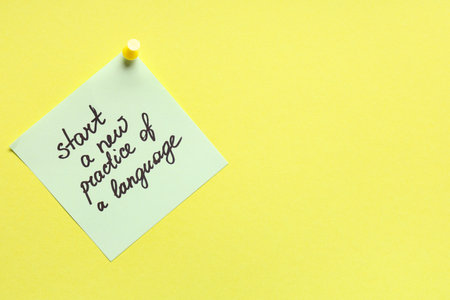 Green sticky note with text START A NEW PRACTICE OF A LANGUAGE on yellow backgroundの写真素材