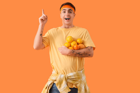 Sporty young man with many fresh oranges and raised index finger on color backgroundの写真素材