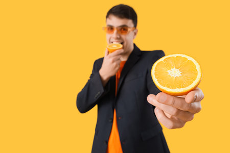Young businessman with fresh orange halves on yellow backgroundの写真素材