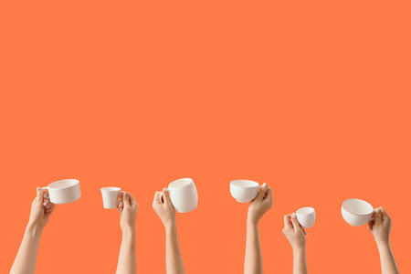 Female hands with different white mugs on orange background
