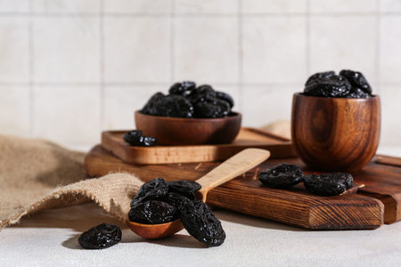 Wooden spoon and bowls with dried prunes on white tableの写真素材