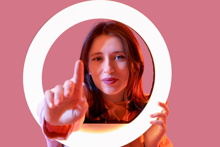 Young woman with ring light using virtual screen on color background, closeup