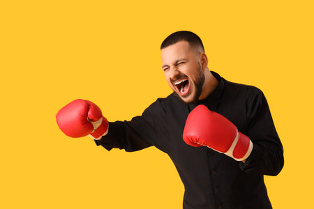 Angry businessman with boxing gloves on yellow background. Knockout concept