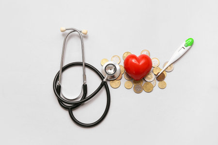 Red heart with coins, thermometer and stethoscope on gray background