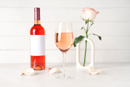 Glass and bottle of pink wine with beautiful rose on white tableの写真素材